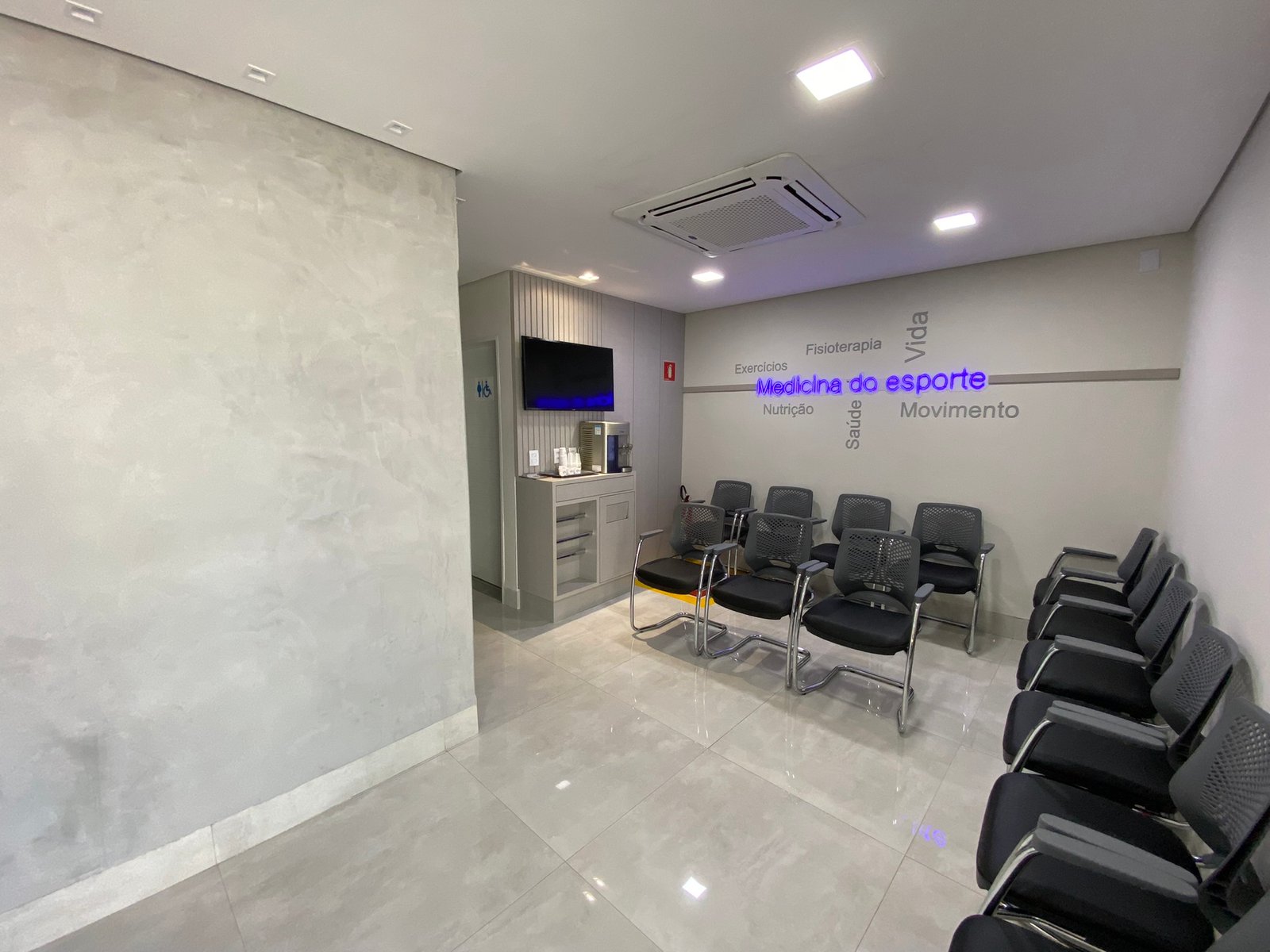 Sala de espera da clínica, com cadeiras, televisão e ambiente climatizado